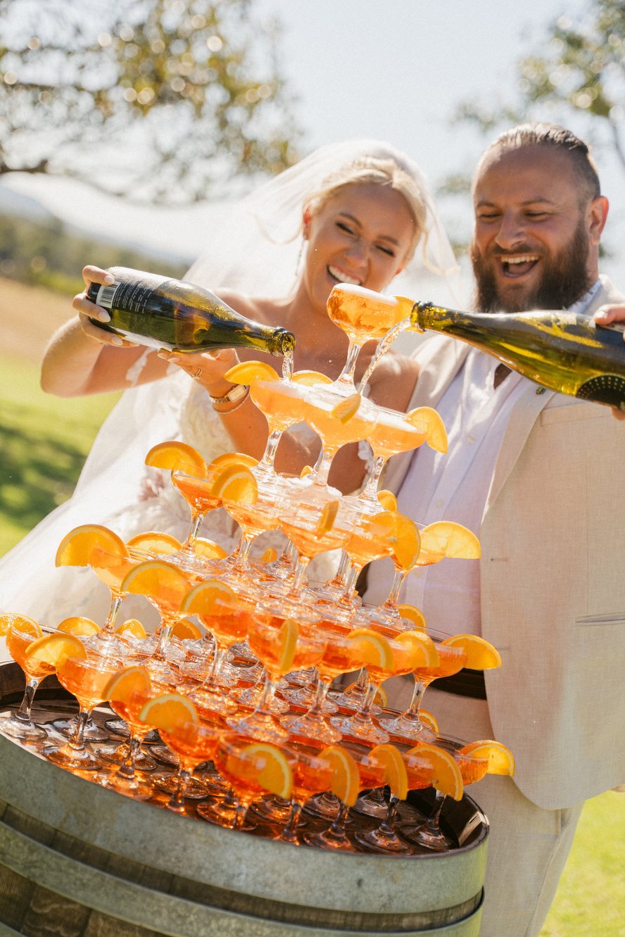 A couple pouring a cocktail tower on the lawn