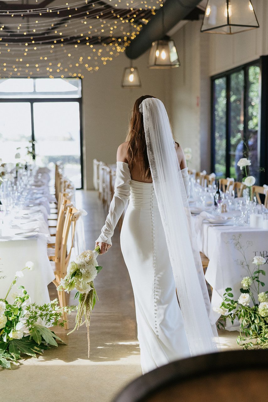 A bride with a long veil walking past the set long tables