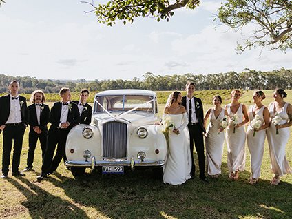 A bridal party with a vintage car under the trees